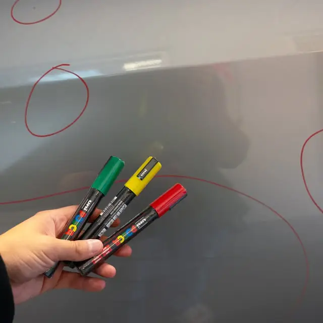 three acrylic paint markers being shown againsrt a grey vehicle